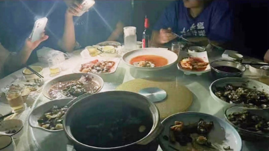 上海餐厅内有客人围坐一桌进餐,桌上7、8道菜,并配有米饭和酒,有人打开手机灯照亮饭桌。(图片来源:微博)